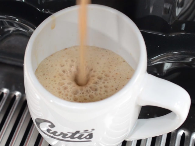 Cappuccino is being dispensed into a coffee mug